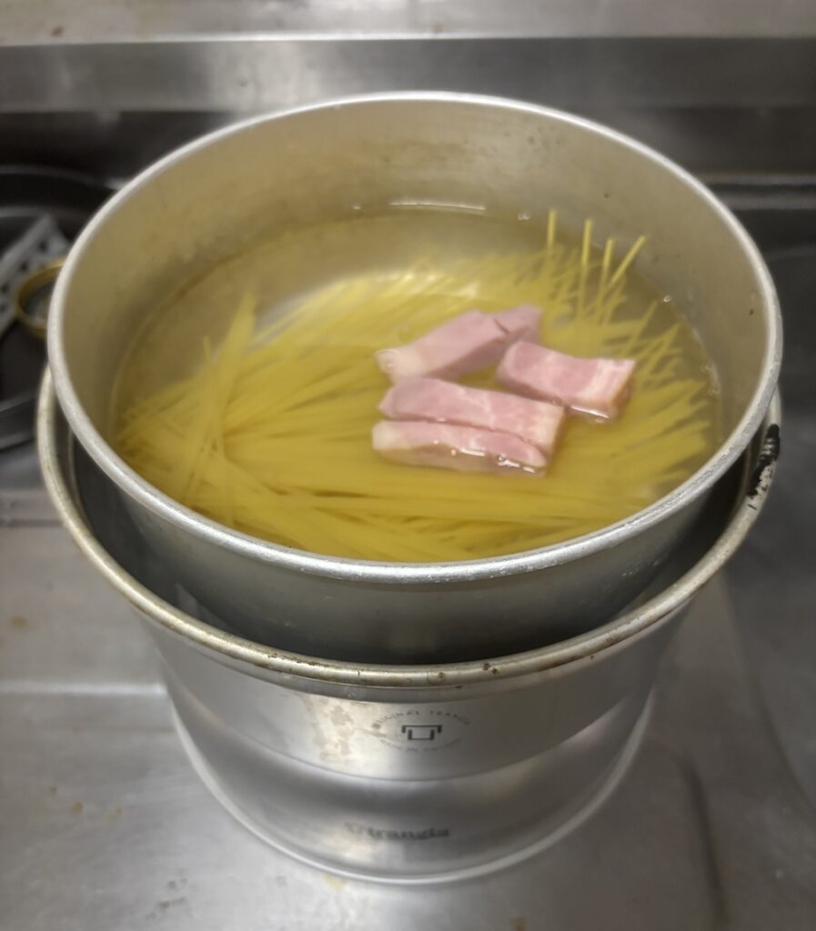 沸騰したお湯にパスタとベーコンを入れる